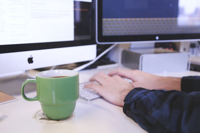 hands on a computer with a green mug